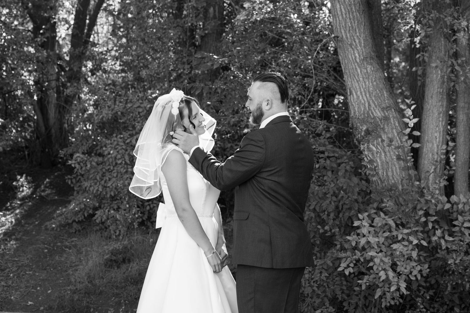 Black and white wedding portrait of couple embracing in a forest setting.