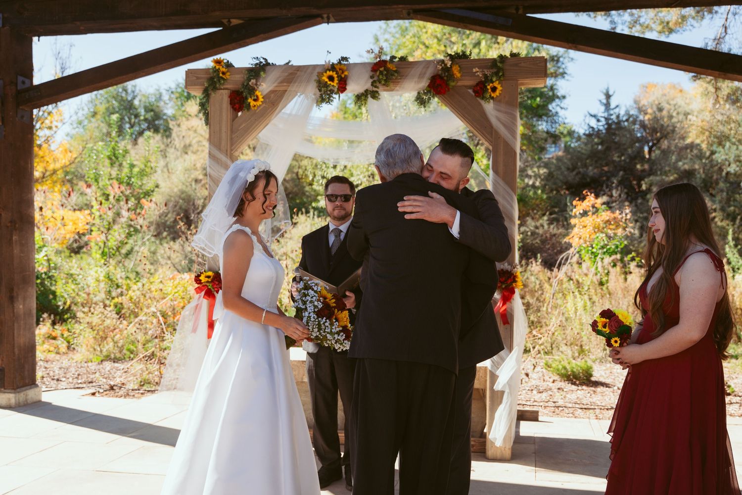 Wedding ceremony under wooden pergola decorated with autumn flowers and greenery.