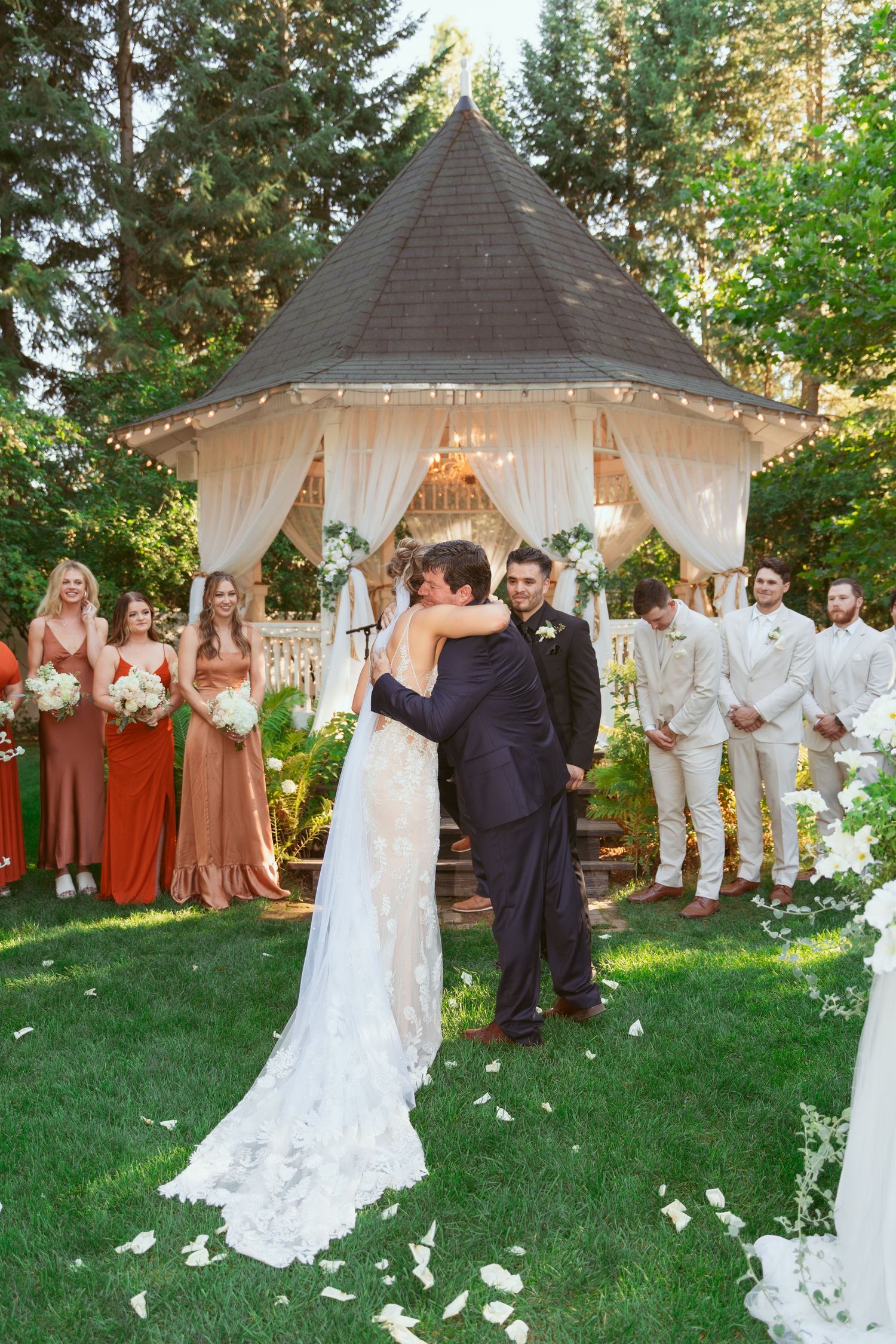 Outdoor wedding celebration with white gazebo decorated in fairy lights and floral arrangements.
