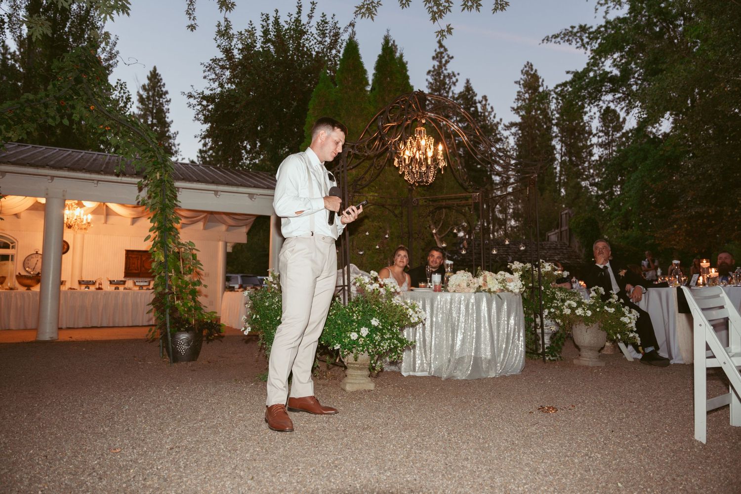 Evening outdoor wedding reception with string lights and decorative white furniture.