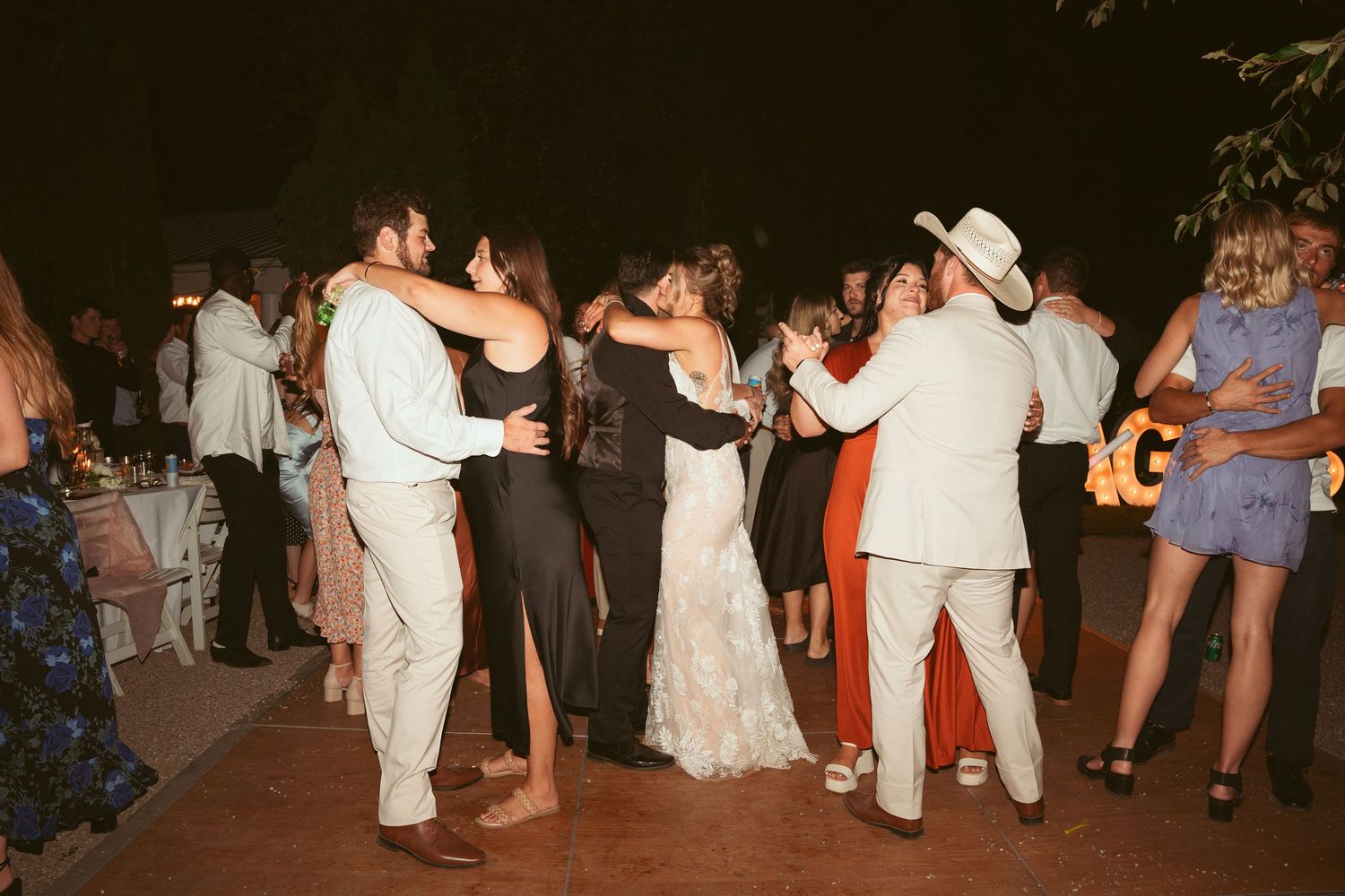 Wedding party dancing in formal attire at an outdoor evening celebration.