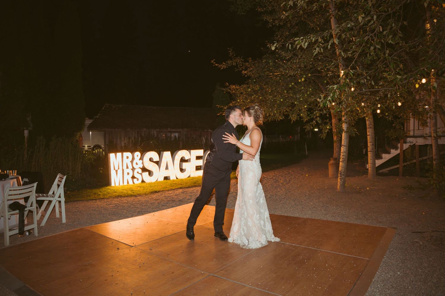 Wedding couple and guests dancing near illuminated MRS sign at outdoor evening reception.
