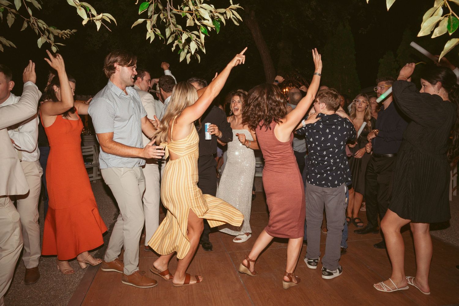 Wedding party and guests dancing in formation during a lively outdoor evening celebration.