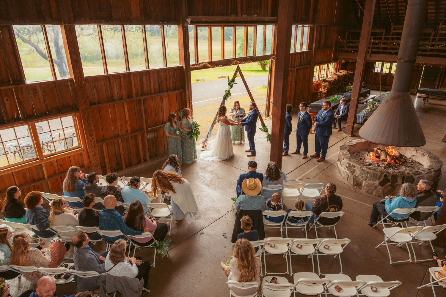 Wide view of rustic barn wedding venue with wooden beams and folding chairs set up for ceremony.