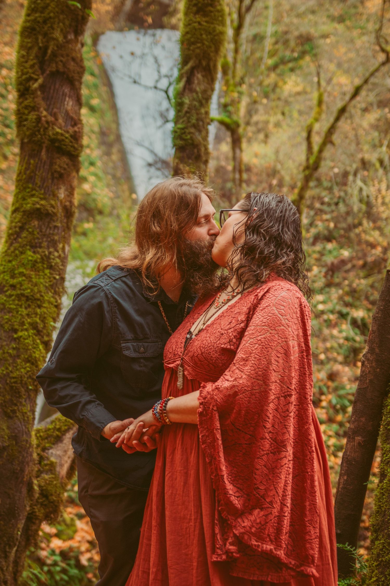 A romantic moment captured against moss-covered trees in a fall forest setting.