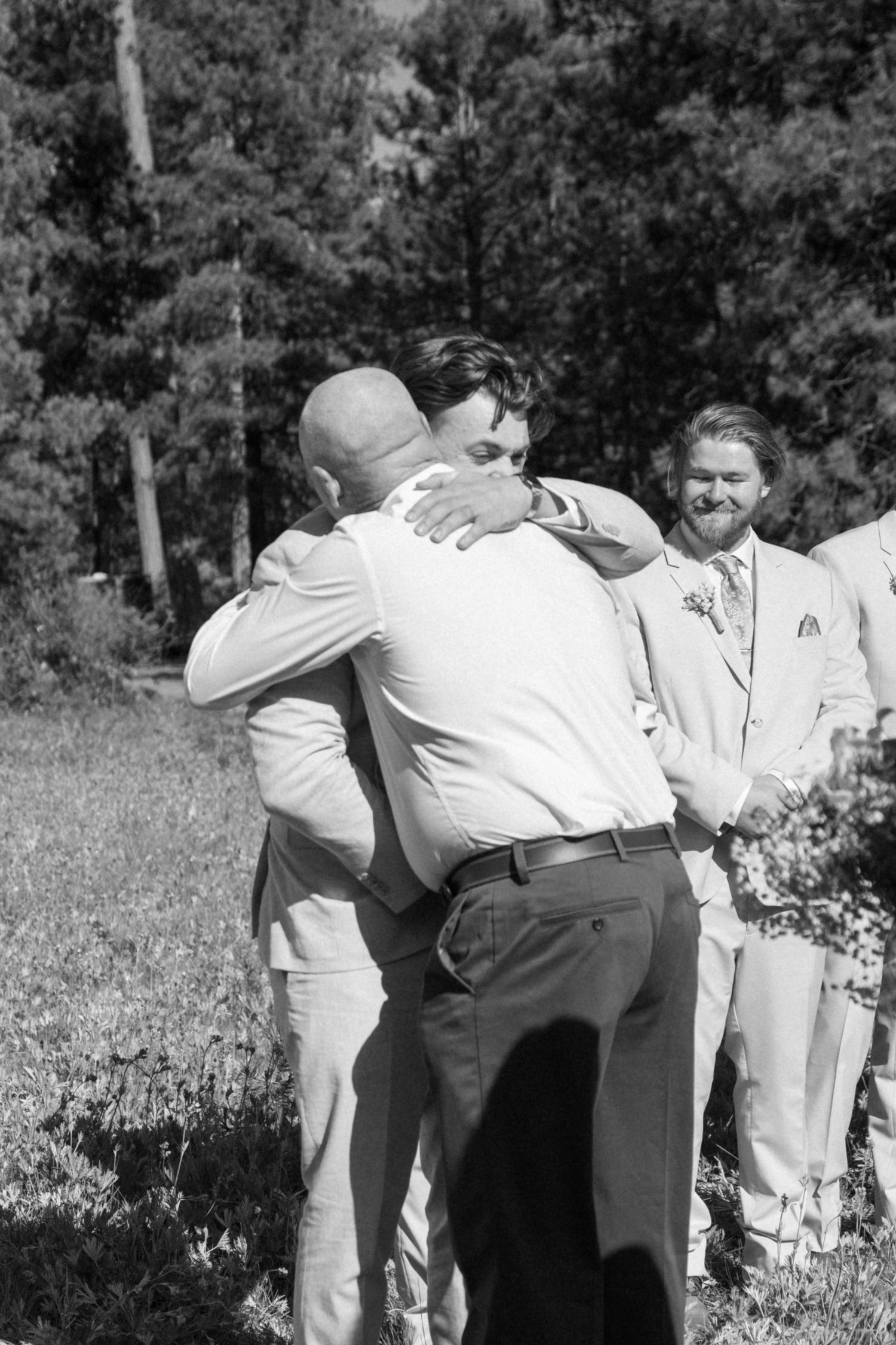 Black and white photo of wedding party members sharing a playful moment outdoors.