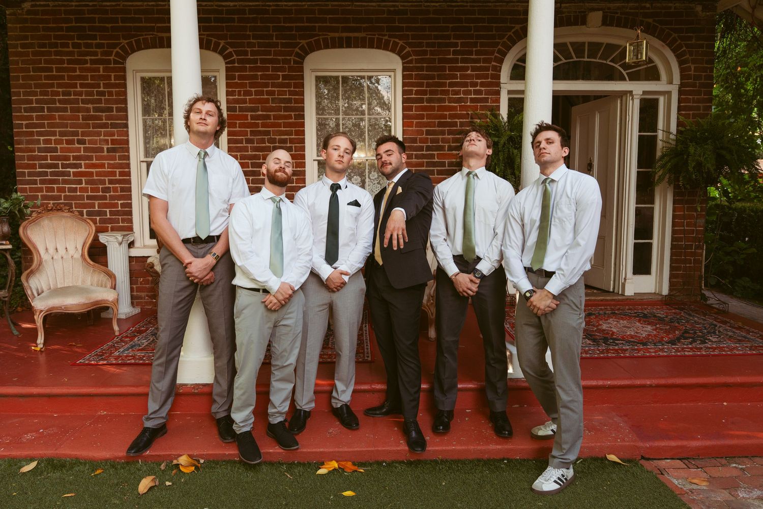 Wedding party groomsmen in light gray suits stand together on red carpet.