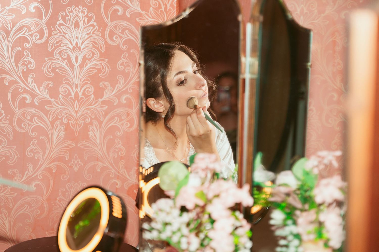 Elegant vanity setup with illuminated makeup mirror and floral arrangements.