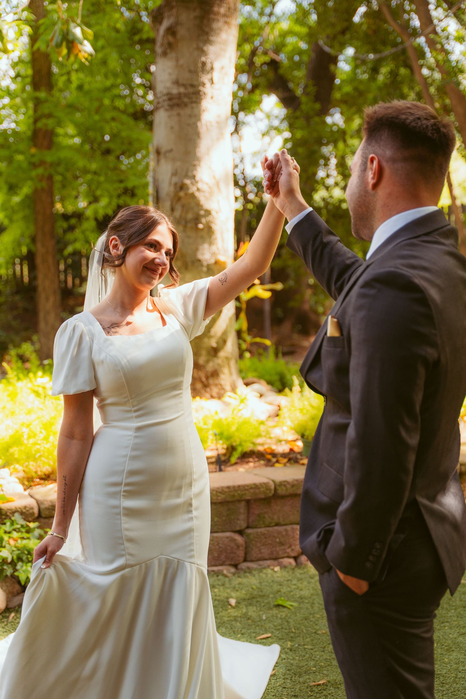 A joyful wedding couple dancing together in a garden setting with lush green trees in the background.