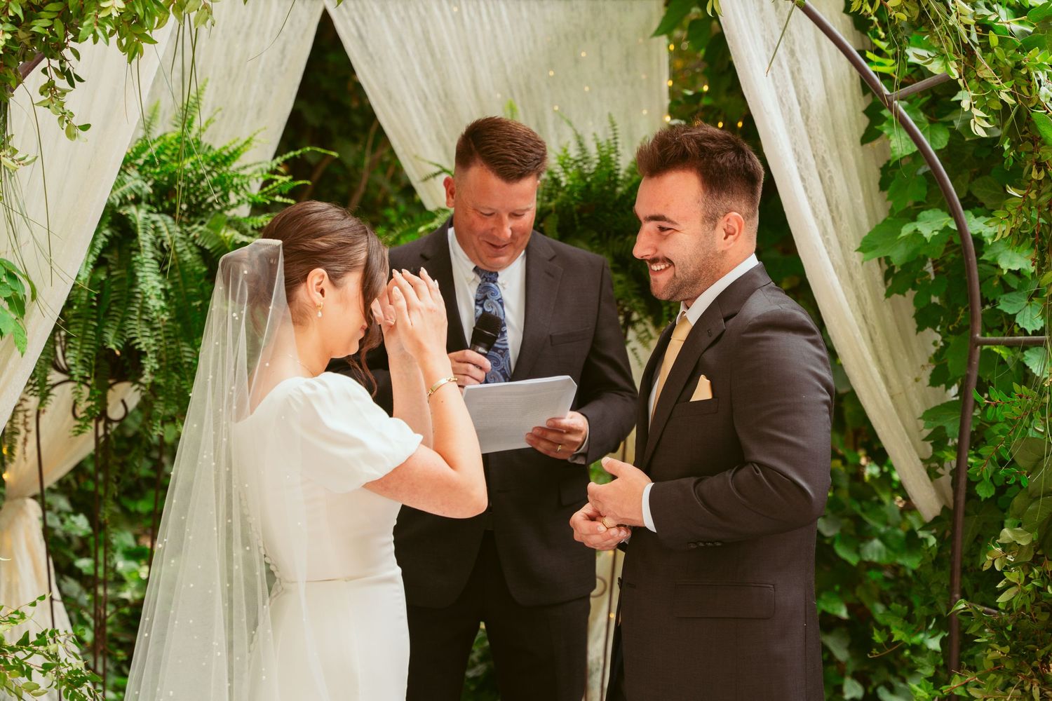 Emotional wedding ceremony moment captured in a garden setting with white fabric draping.