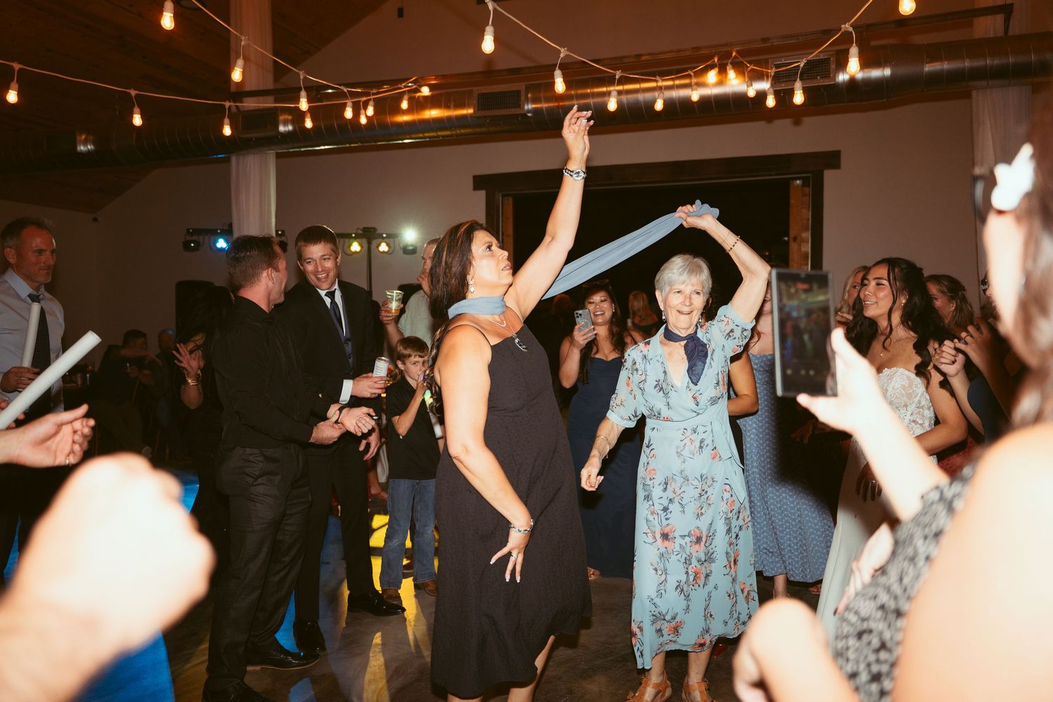 Energetic dance party with guests raising their hands under string lights at an indoor venue.