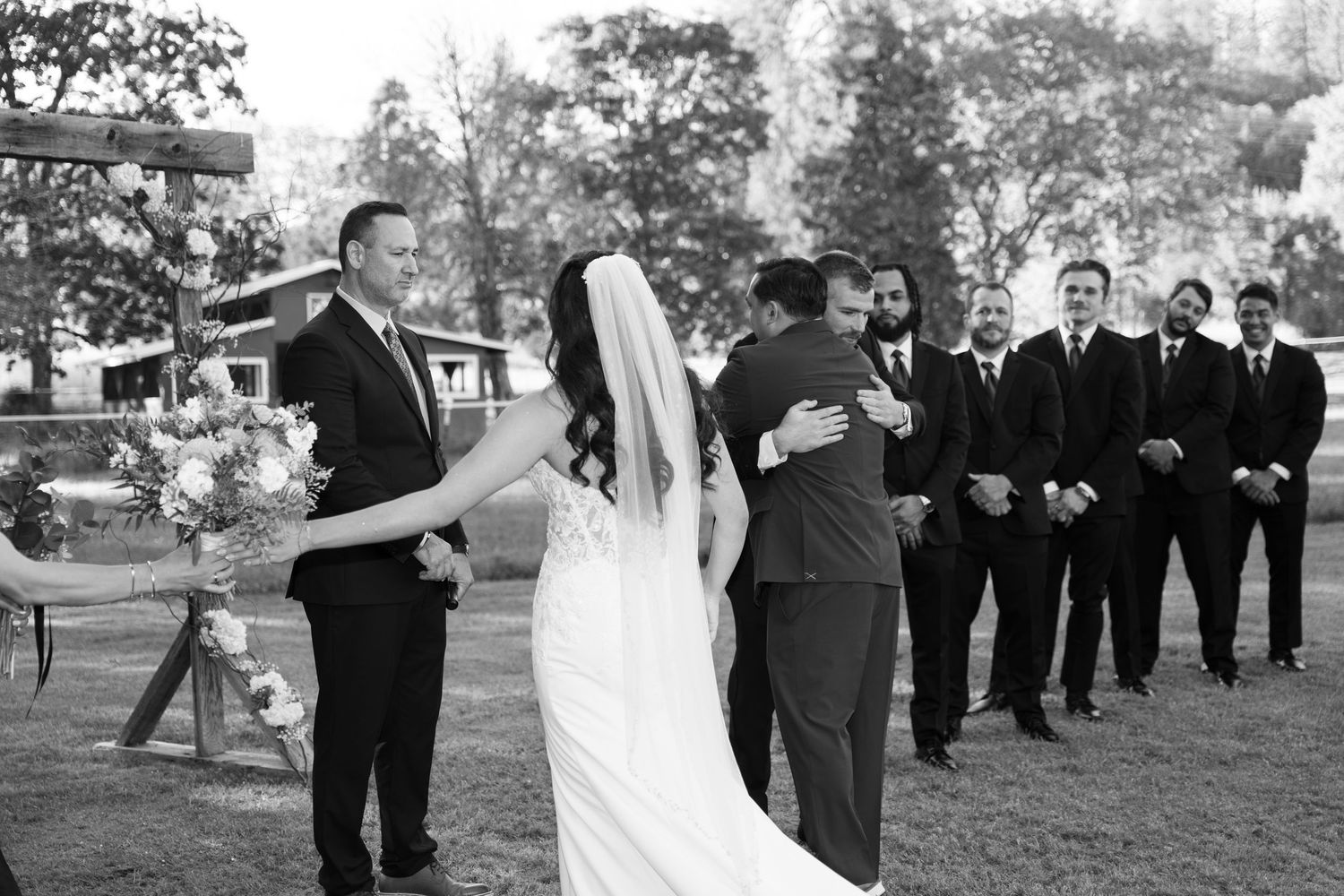 Black and white photo of wedding party posing outdoors in formal attire.