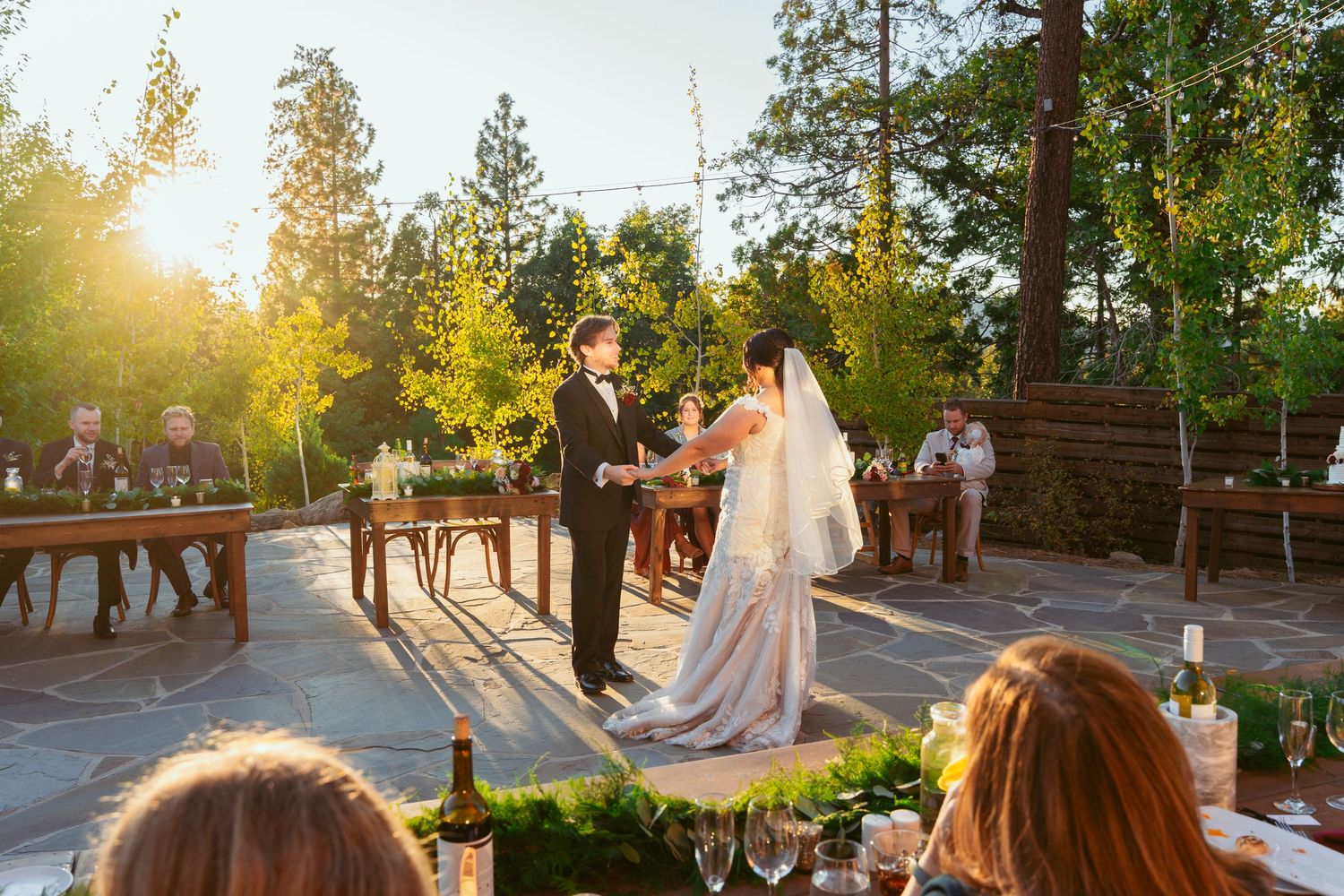 Wedding ceremony setup outdoors with wooden benches and trees during golden hour sunset.