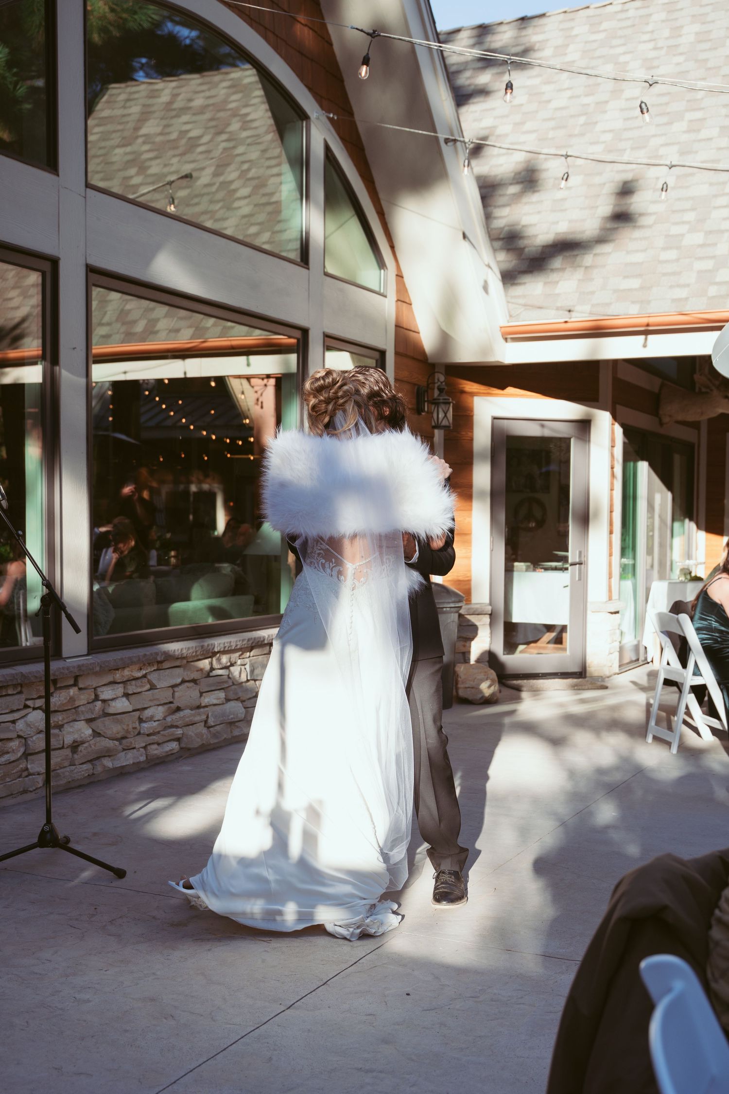 A couple dances together on a patio with string lights and modern architecture in the background.