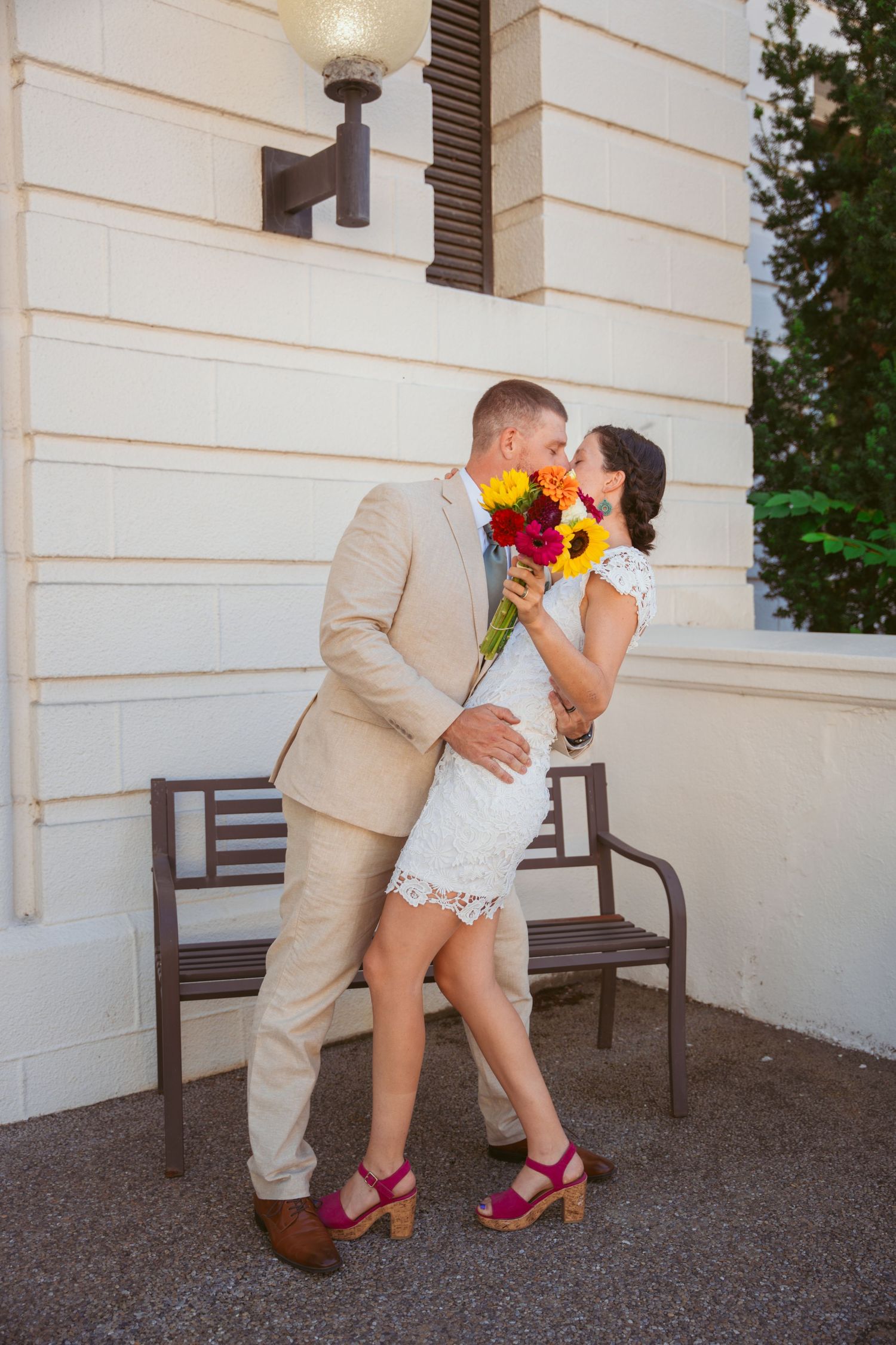 Playful wedding couple sharing romantic moment with colorful bouquet outdoors.