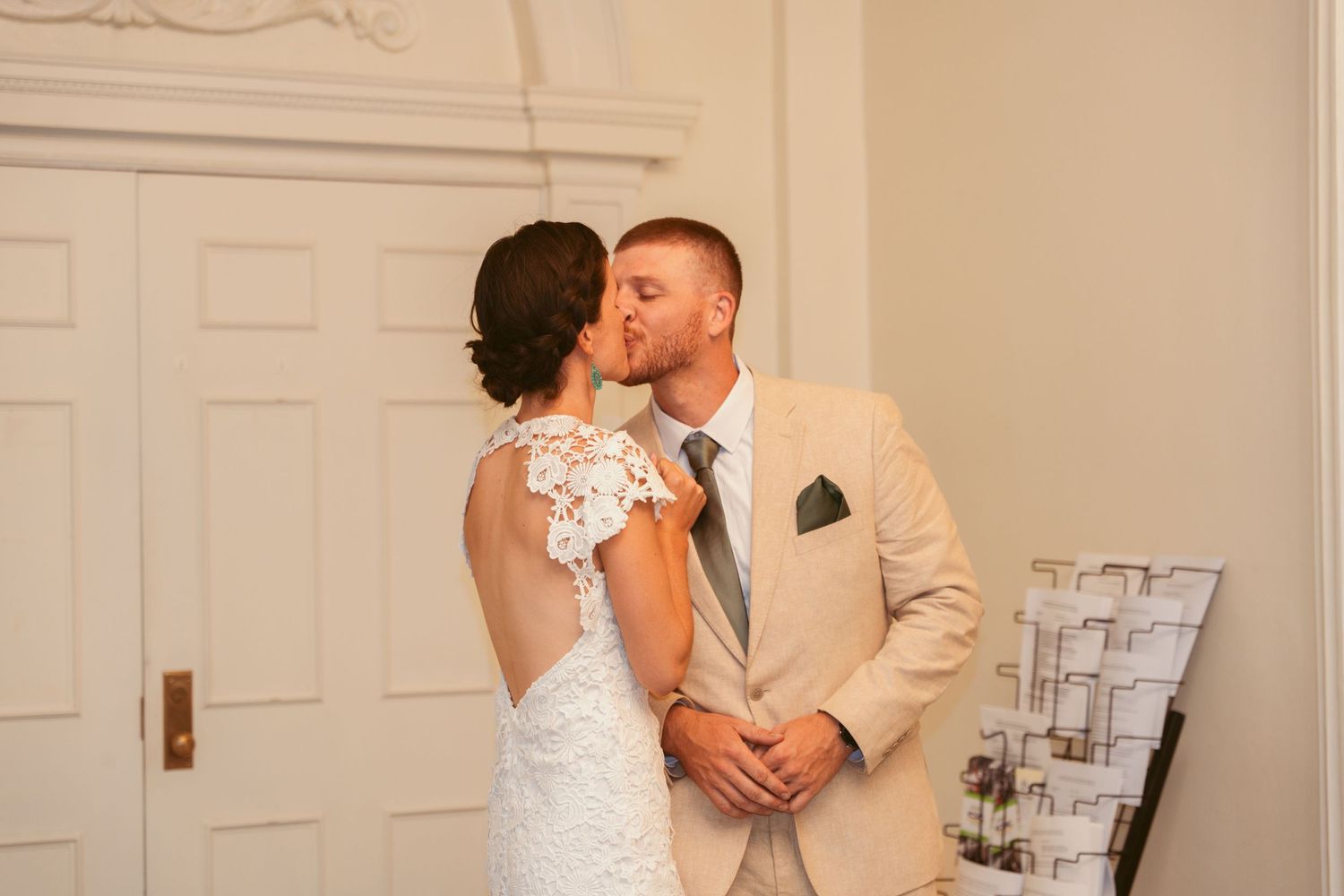 A couple shares a tender moment in front of ornate white wall panels.