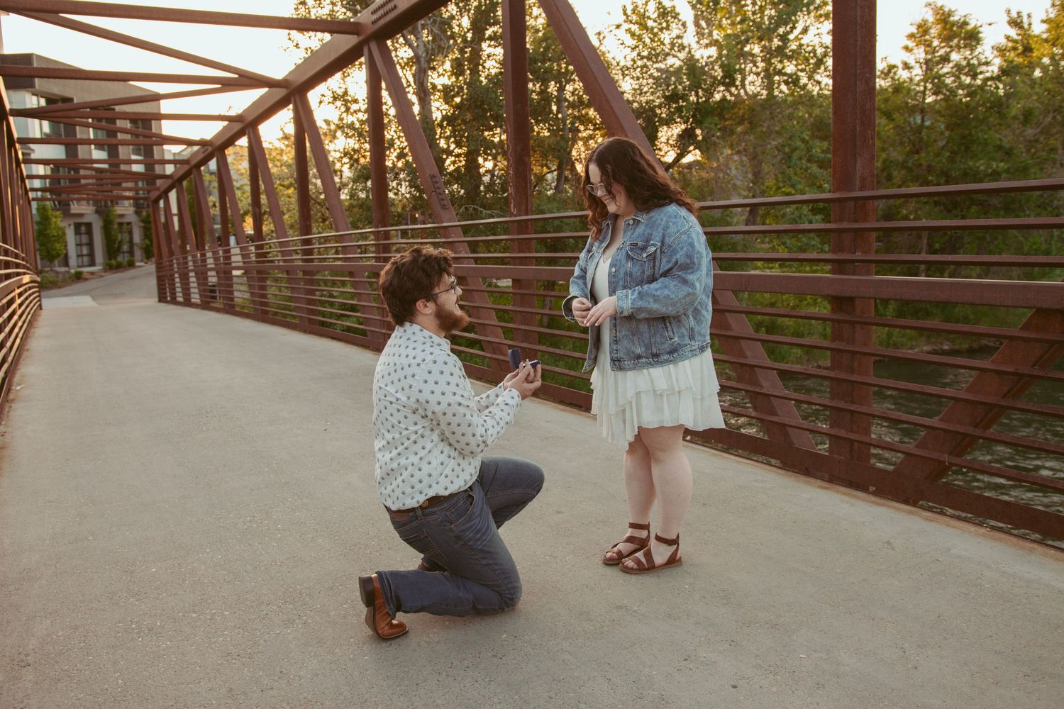 A couple sits and interacts on a modern bridge structure at sunset.