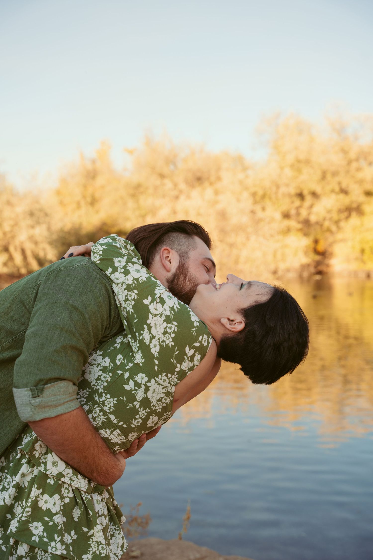 A couple shares a romantic dip kiss against a backdrop of golden sunlit water.