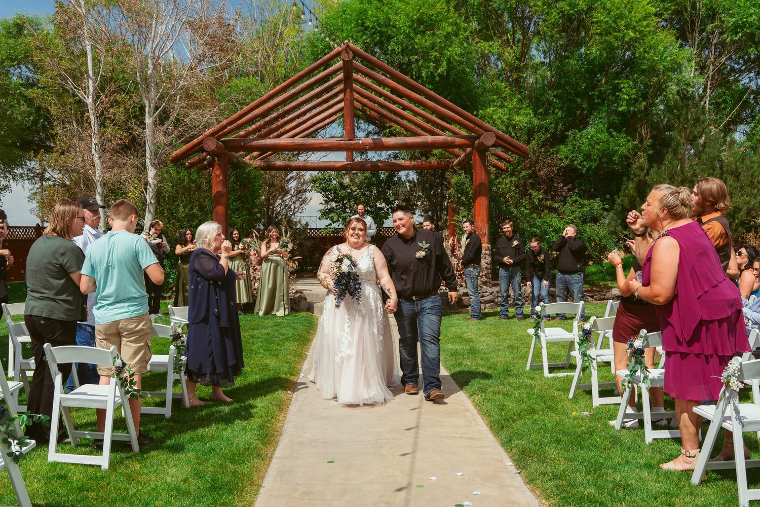 Rustic outdoor wedding venue with wooden pergola and white chairs arranged on grass for ceremony.