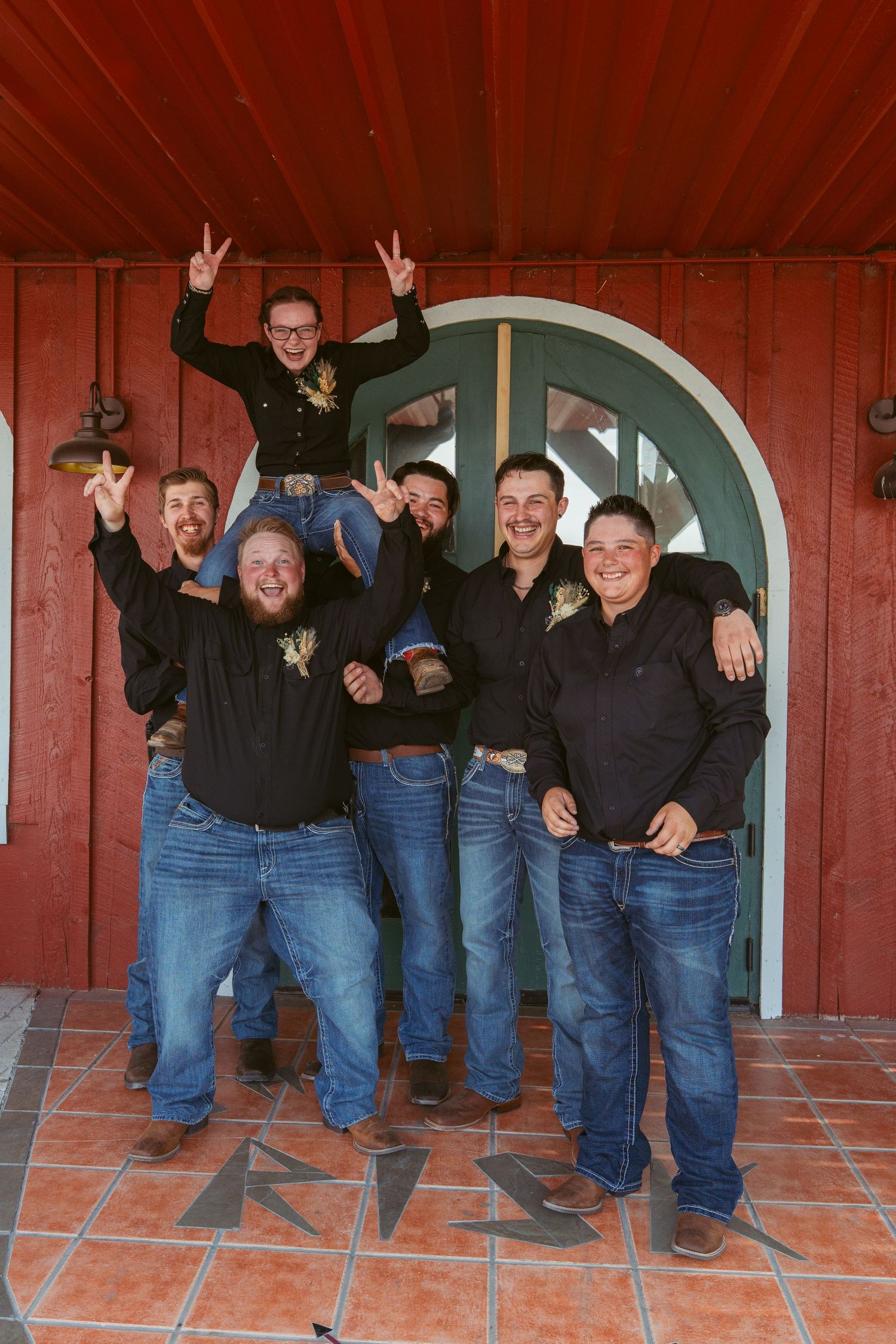 Group photo of friends posing and making silly gestures in front of red building with arched door.
