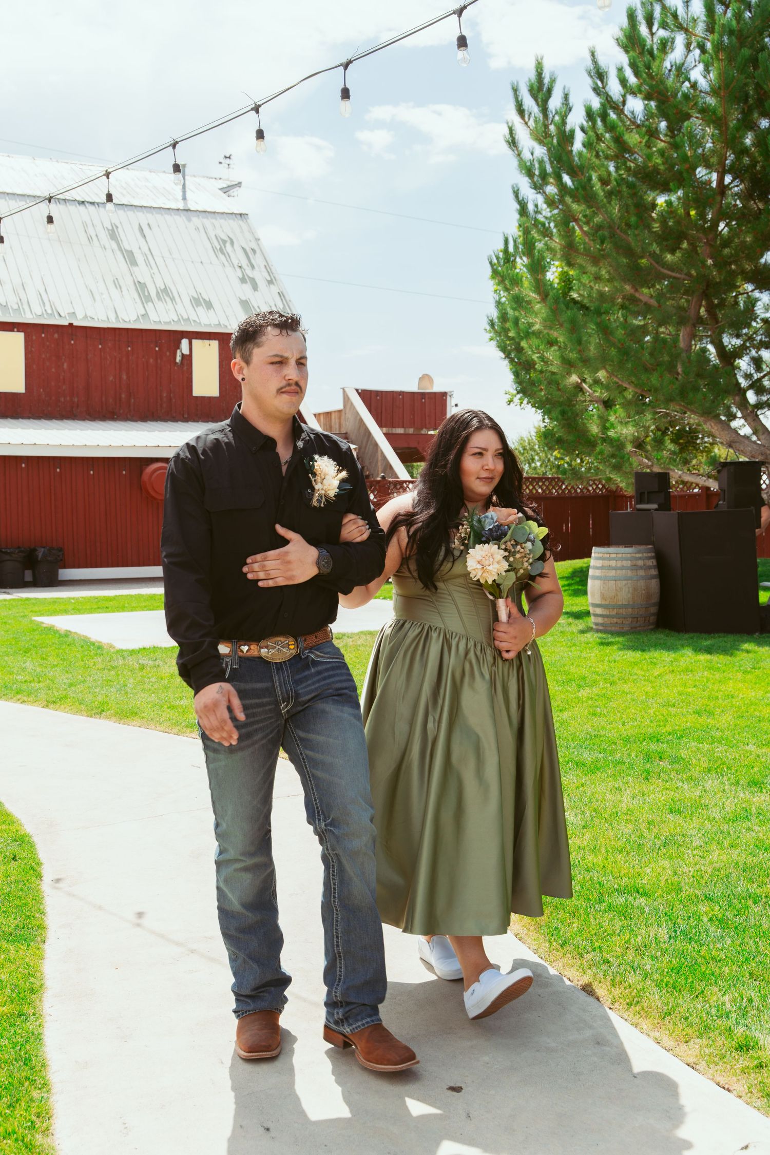 People enjoying a casual moment on a paved pathway near a red barn at an outdoor event.