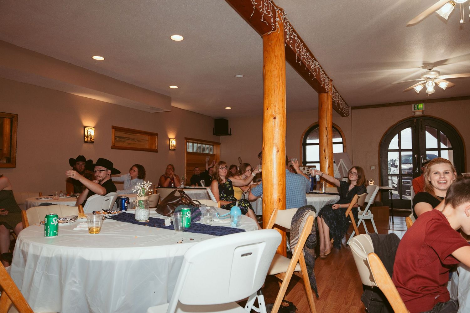Wedding reception venue with guests seated at round tables and wooden architectural details.