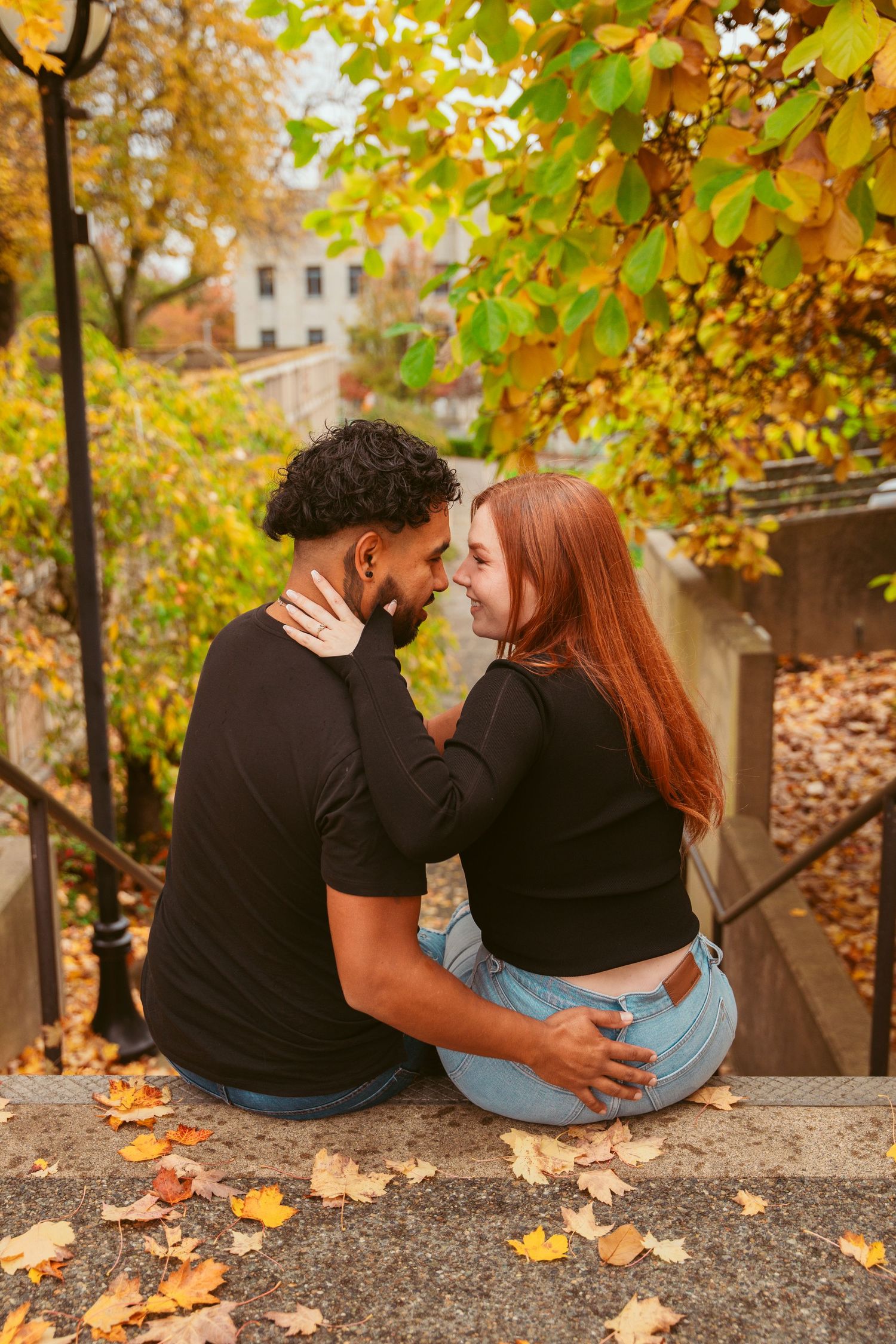 Couple sitting close together on stone steps with autumn leaves scattered around them.