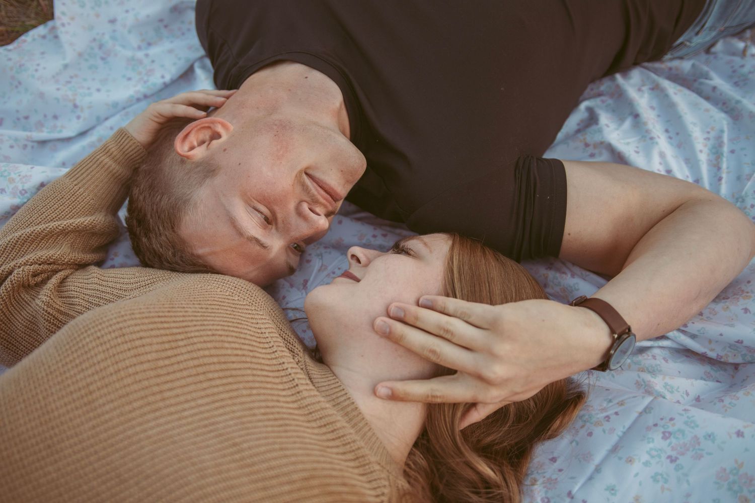 Couple sharing intimate moments lying down together on floral bedding.