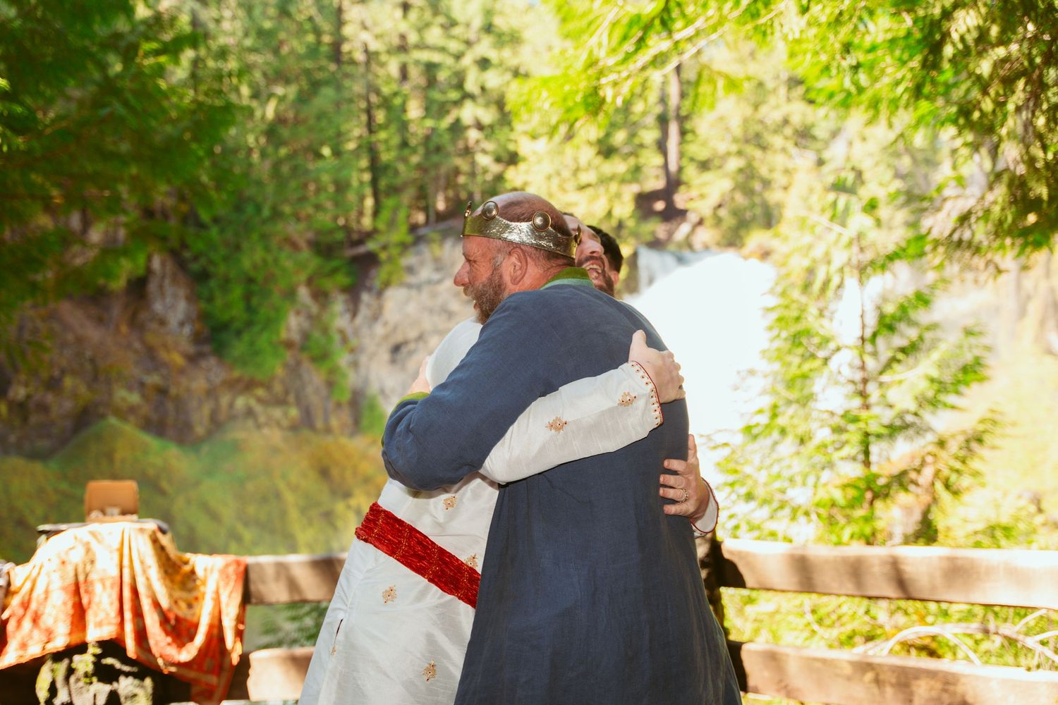 Wedding guests embrace in a sunlit forest clearing during a medieval-themed celebration.