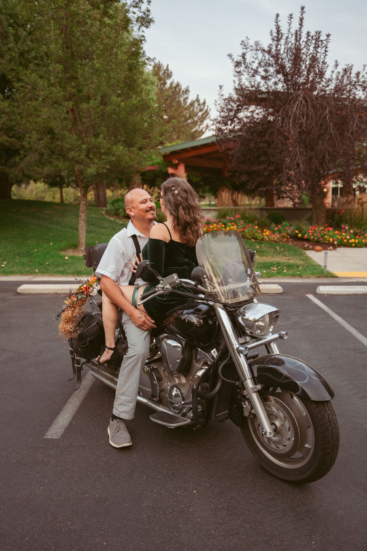 A couple poses playfully with a motorcycle in a parking lot during a photo session.