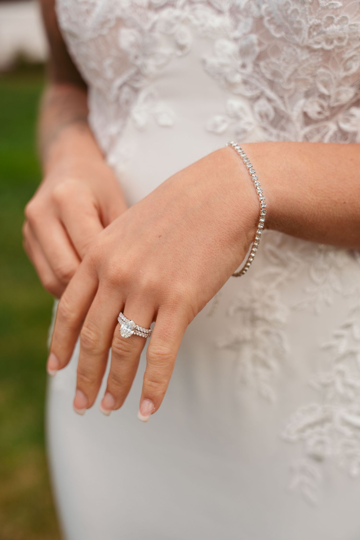 Close-up of bridal jewelry featuring a tennis bracelet and engagement ring with lace dress details.