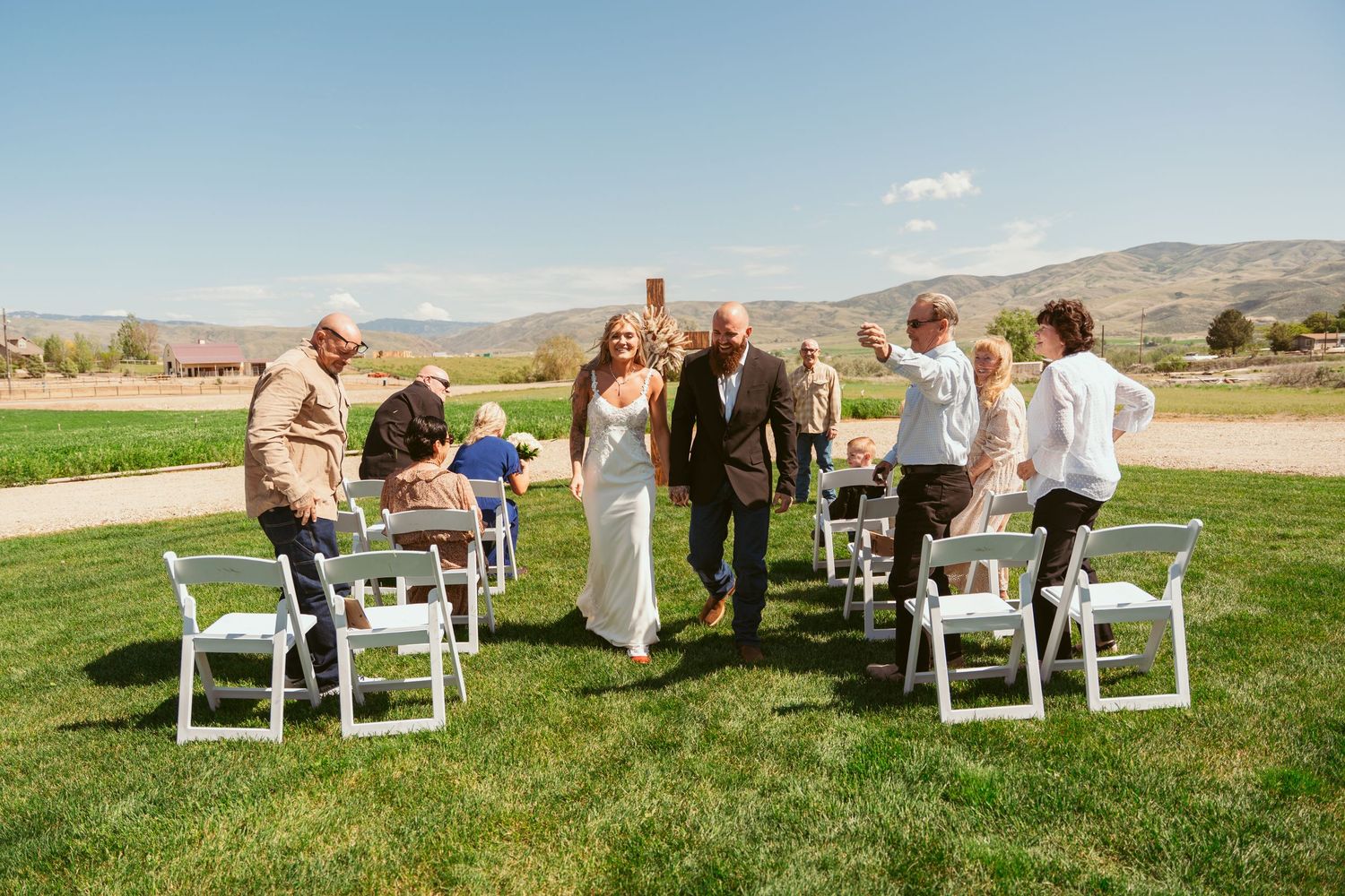 White chairs arranged on green grass for an outdoor wedding ceremony with mountains visible.