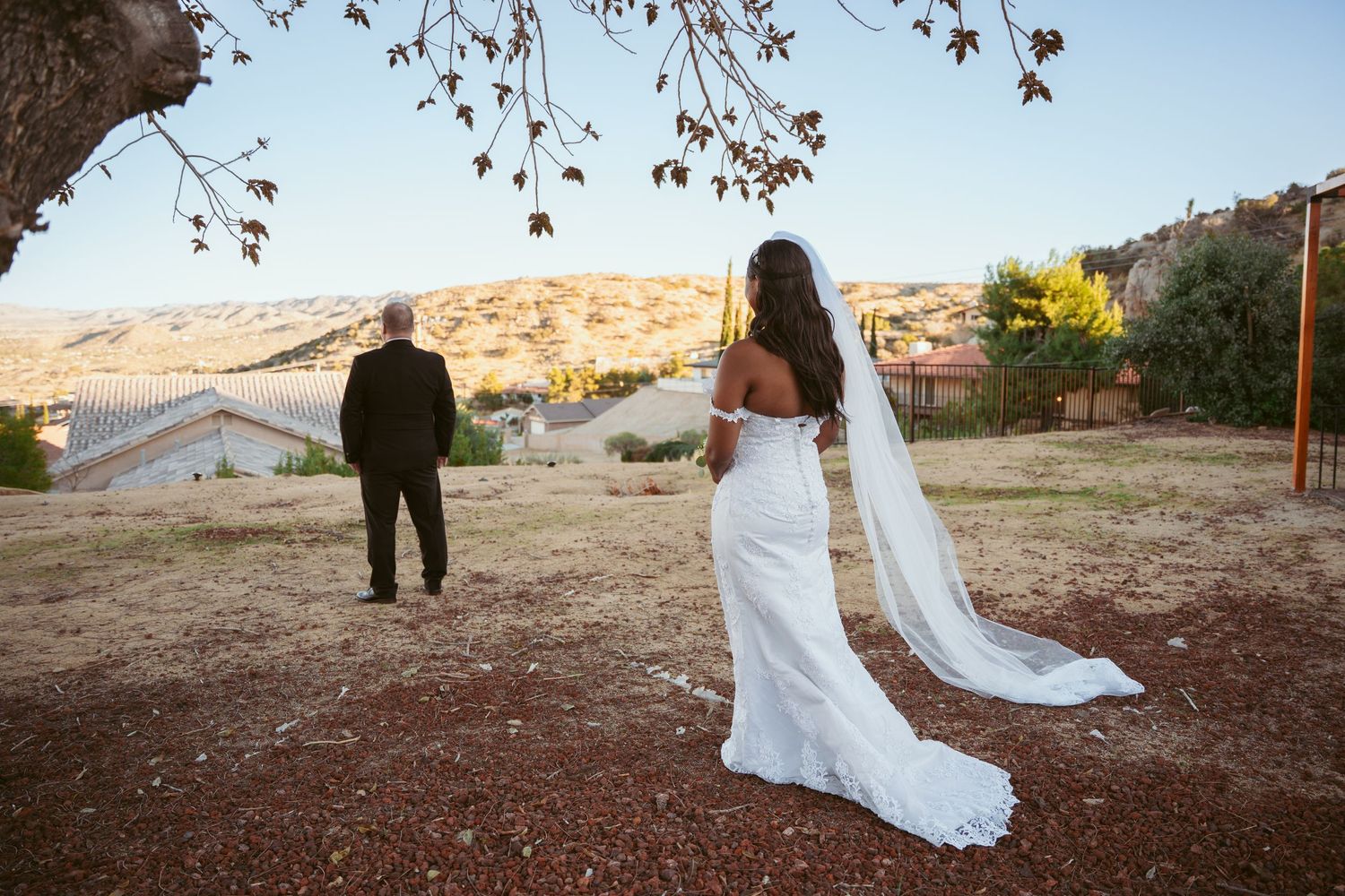 Bride in flowing white dress walking across desert landscape during sunset ceremony.