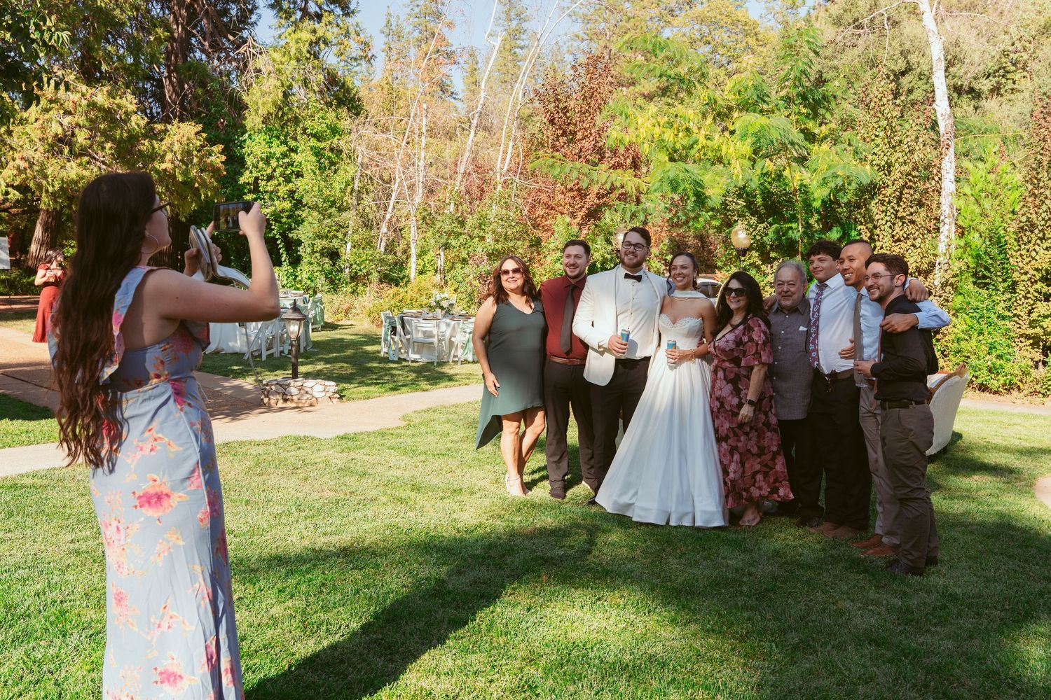 Wedding party dancing outdoors in a garden setting with trees and greenery in the background.