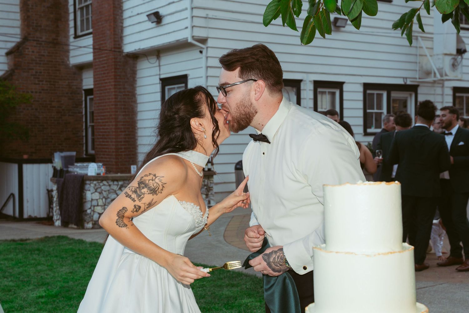 Wedding celebration scene with elegant white cake and couple embracing outdoors.