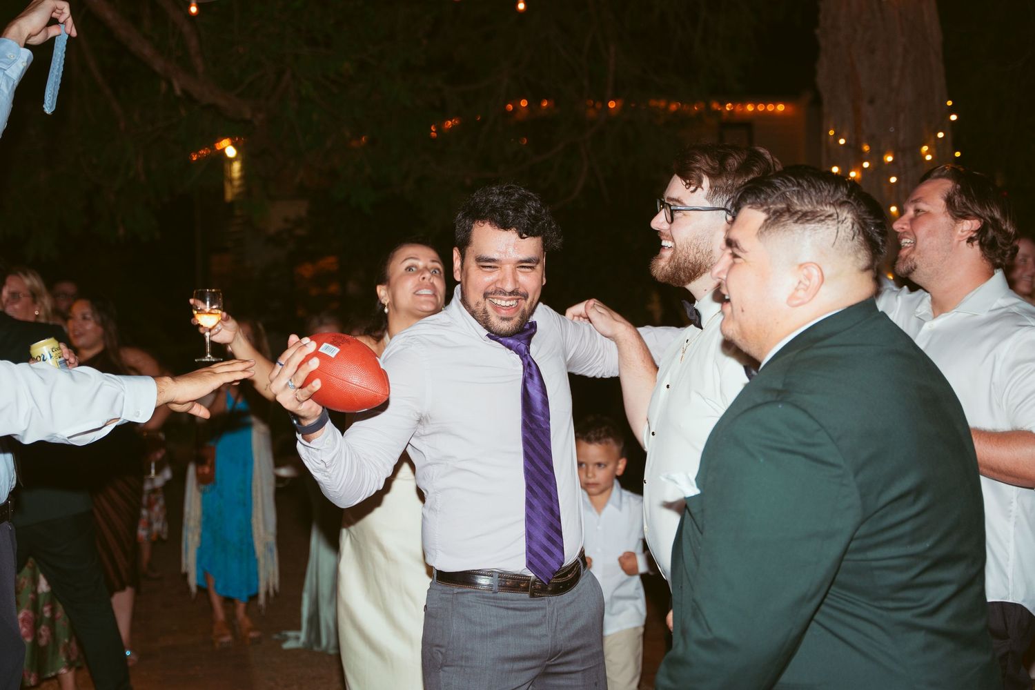 Wedding guests dancing and celebrating on a dimly lit outdoor dance floor under string lights.