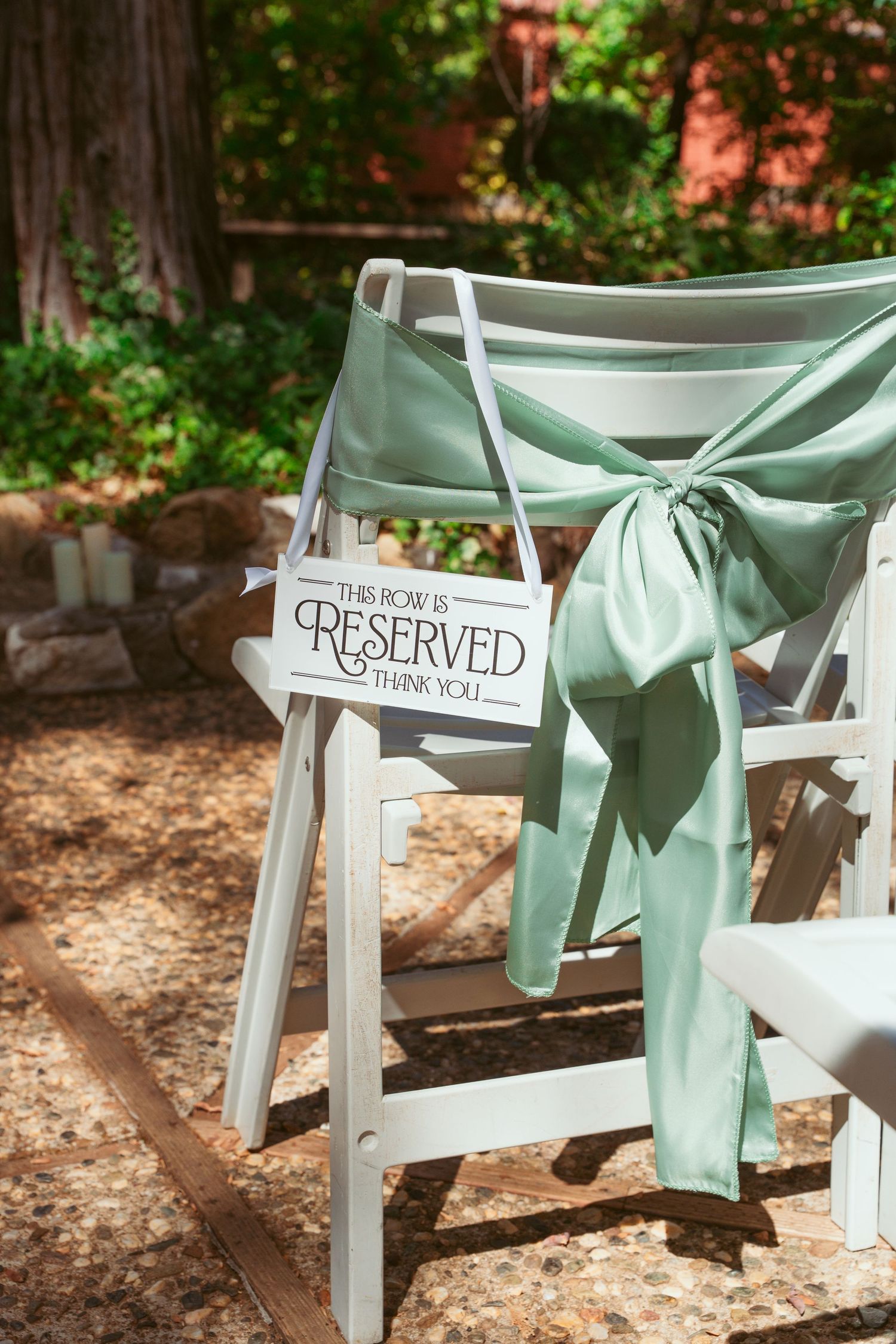 White wooden chairs with mint green sashes and reserved signs set up for an outdoor wedding ceremony.