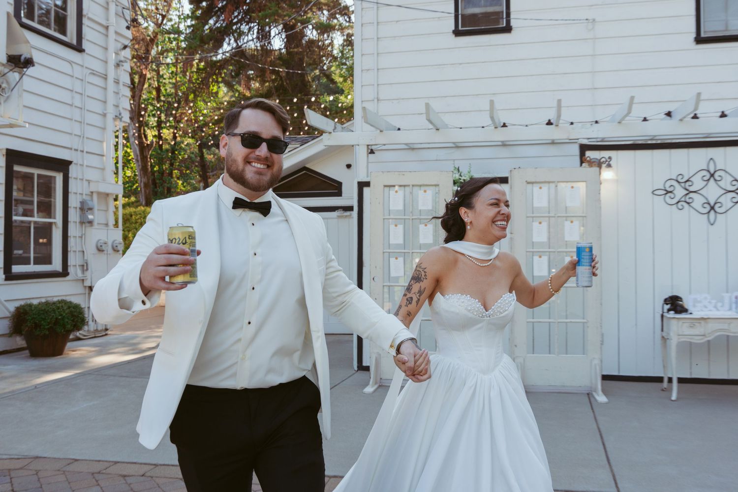 Wedding party members pose playfully outside white building during daytime celebration.