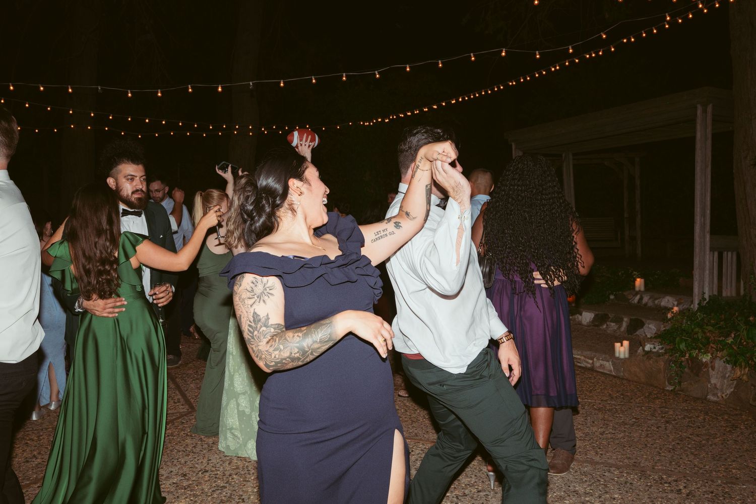 Wedding guests dancing under string lights at outdoor evening reception.