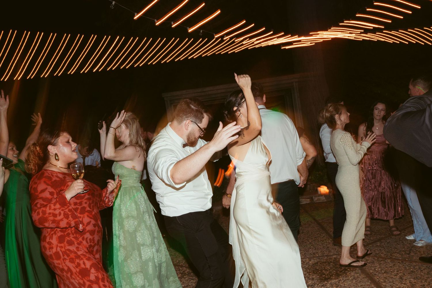 Party guests dancing under warm orange lighting at a nighttime celebration event.