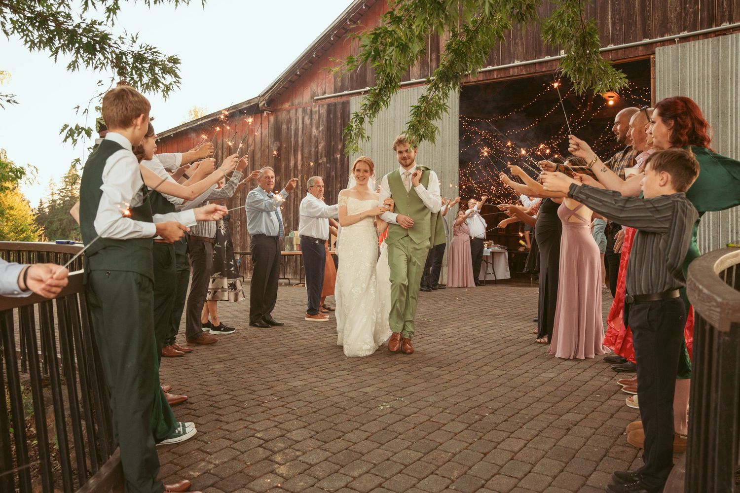 Sparkler exit celebration with guests in formal attire outside rustic barn wedding venue.