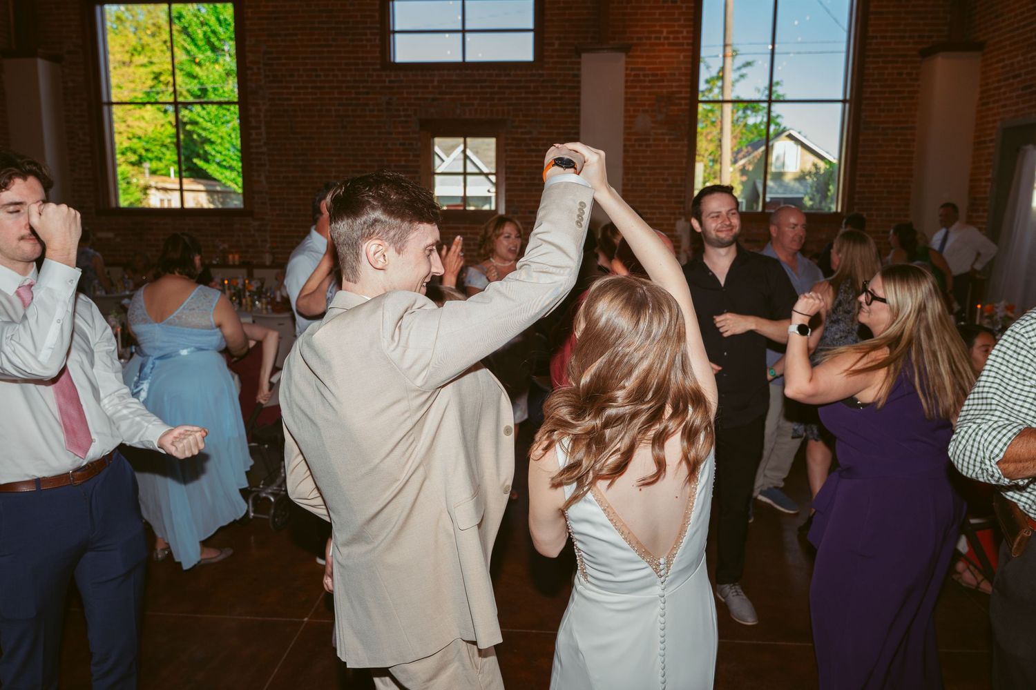 Wedding guests dancing and celebrating under string lights in a rustic indoor venue.