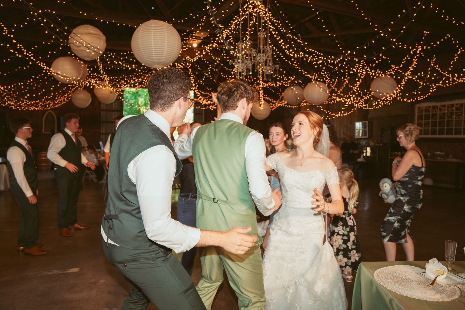 Wedding celebration in full swing with guests dancing under romantic barn lighting.