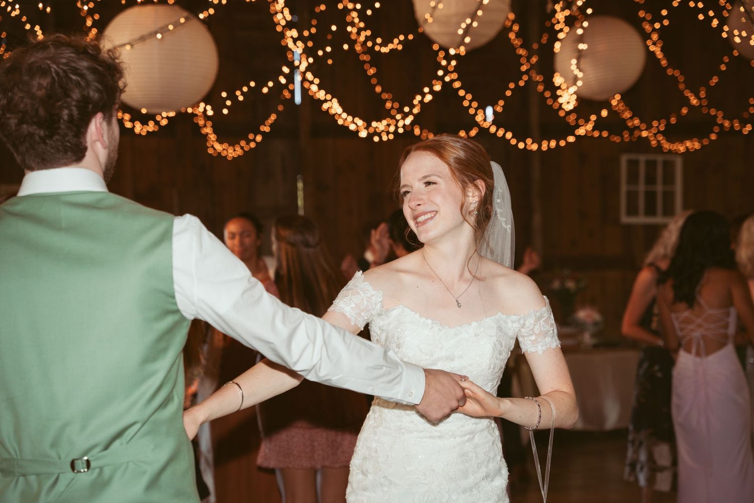 Couples dancing at a wedding reception under warm glowing string lights and paper lanterns.