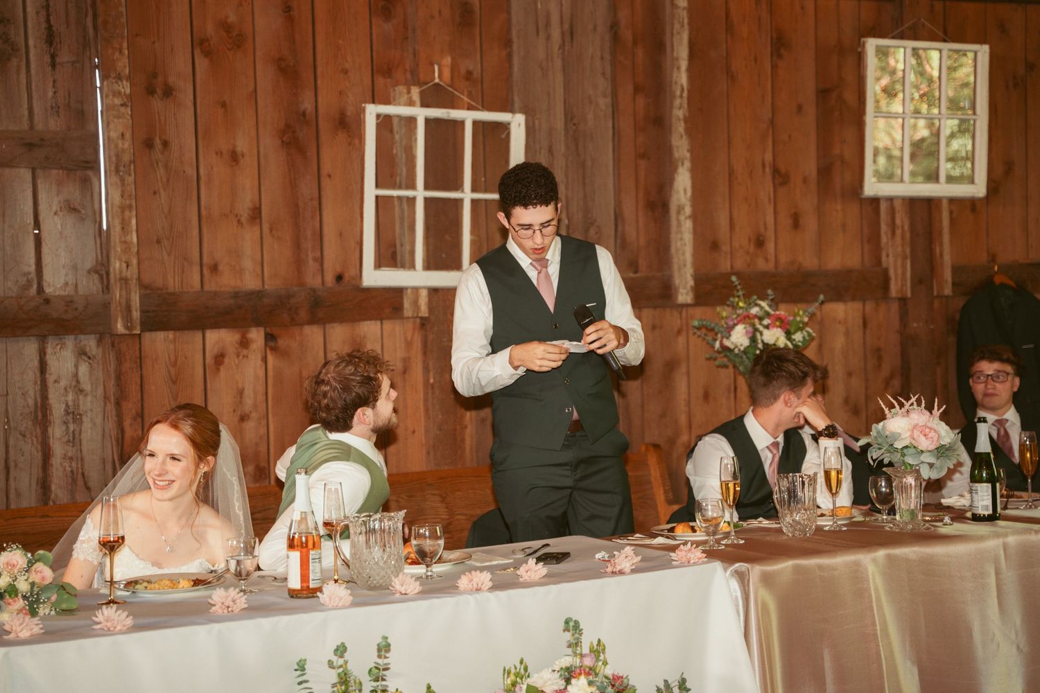 Wedding reception speech moment in rustic barn venue with decorated head table.