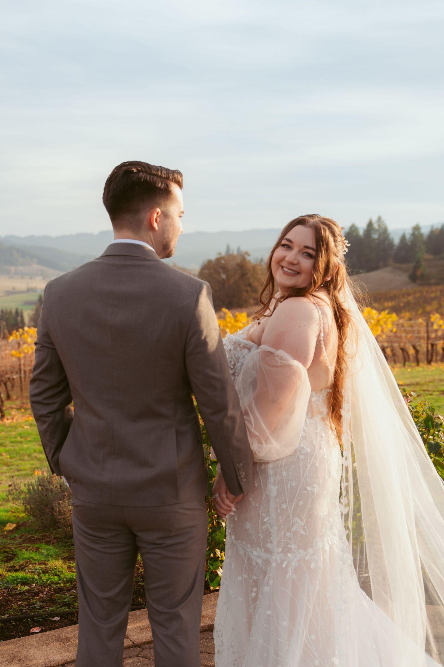 A romantic wedding couple poses in a vineyard during autumn with golden foliage in the background.