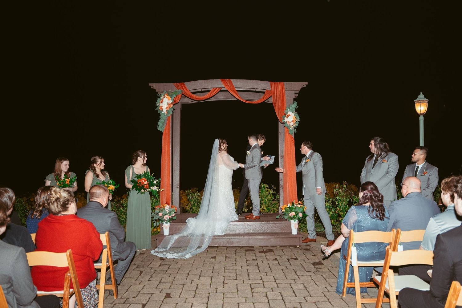 Wedding guests seated outdoors at night with illuminated gazebo in background.