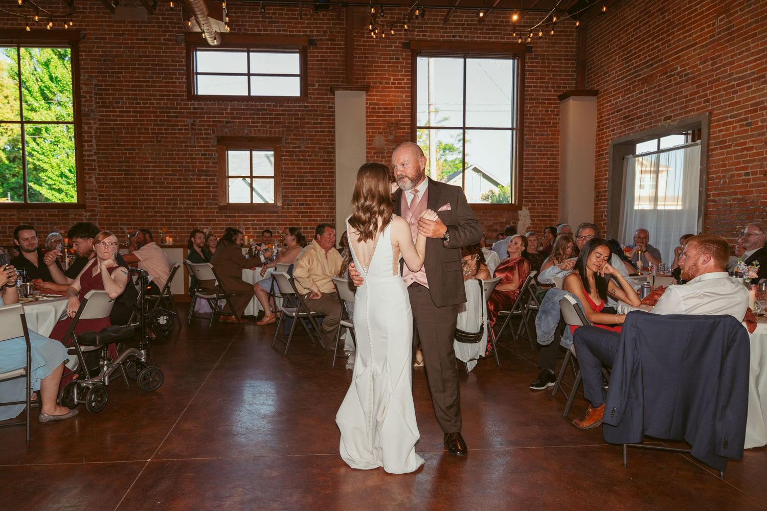Dancers performing in a spacious brick-walled reception hall with natural lighting.