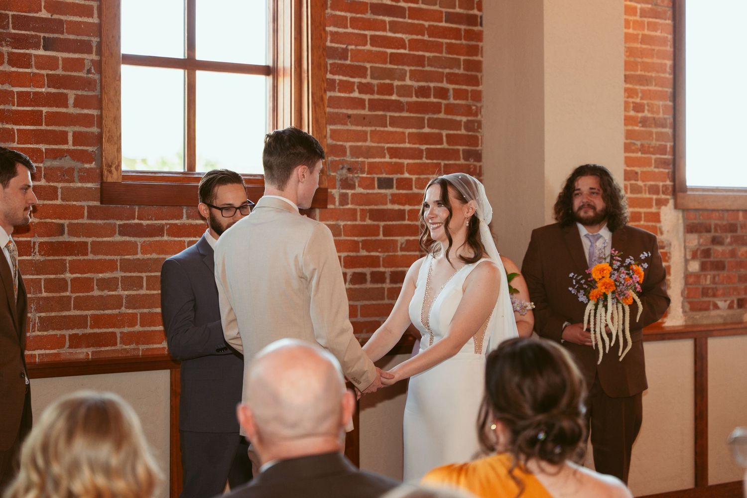 Wedding celebration unfolding in sunlit brick venue with gathered guests and wedding party.