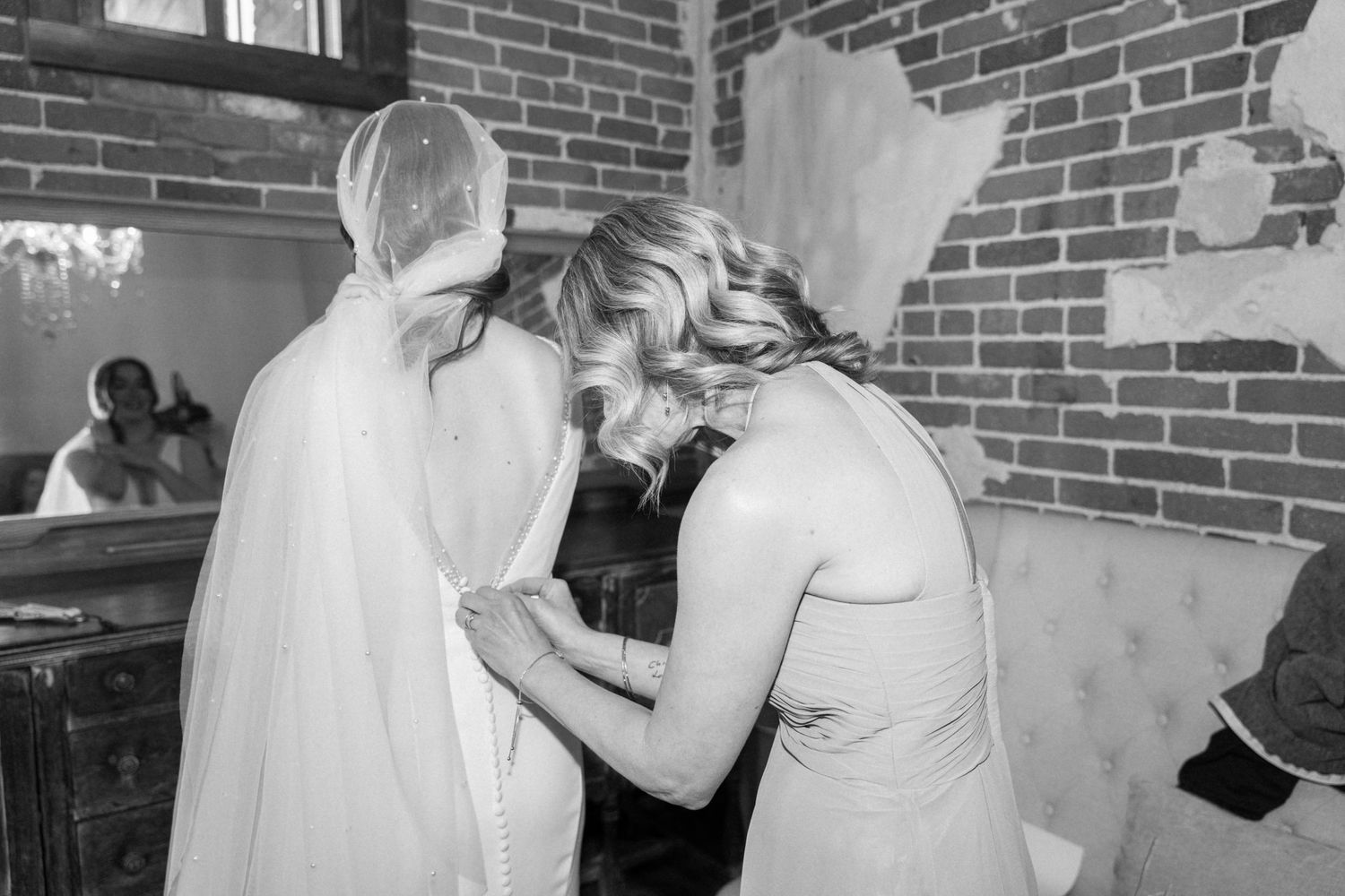 Wedding preparations with bridesmaids helping adjust dress in industrial space.